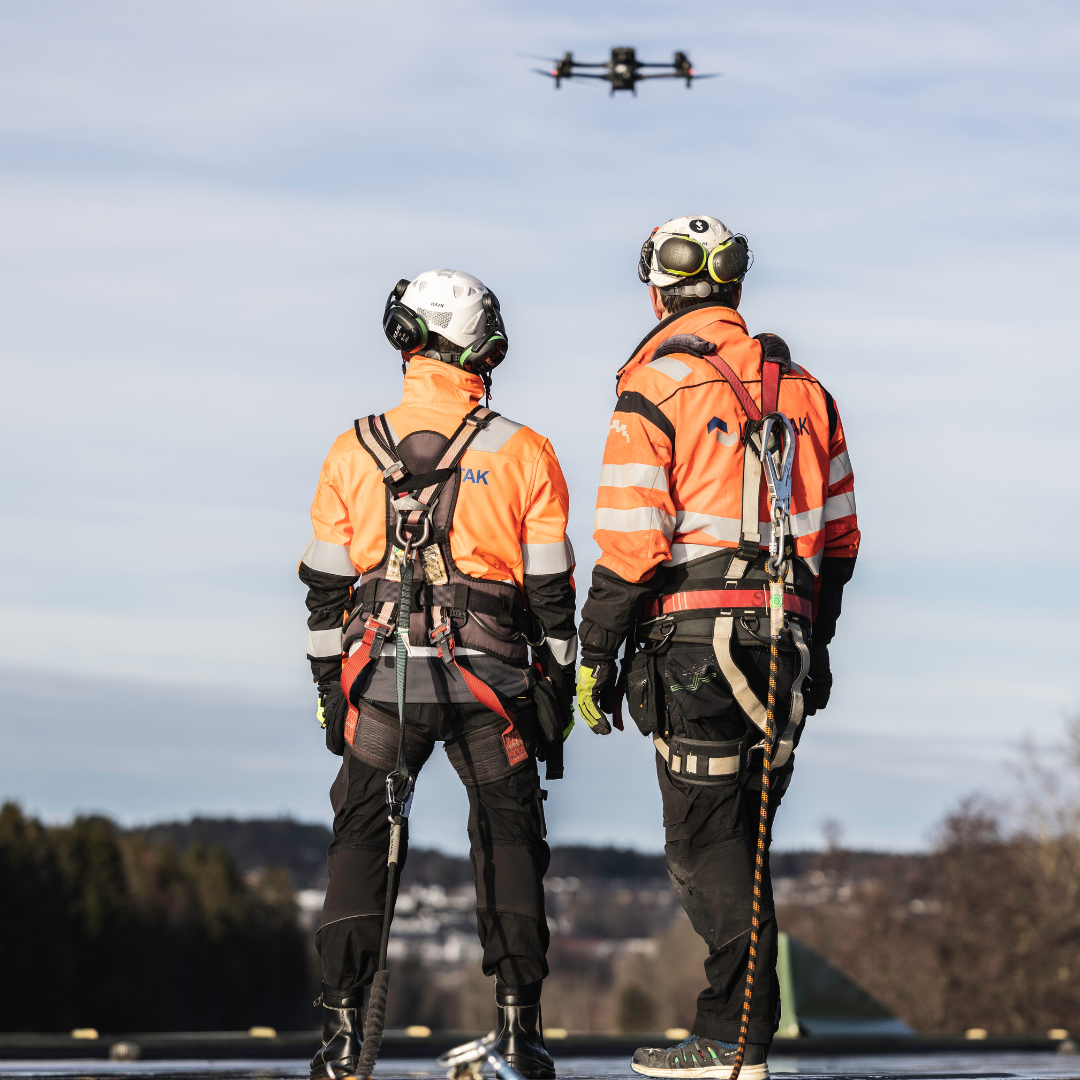 To menn i arbeidsklær oppe på et tak ser på en drone