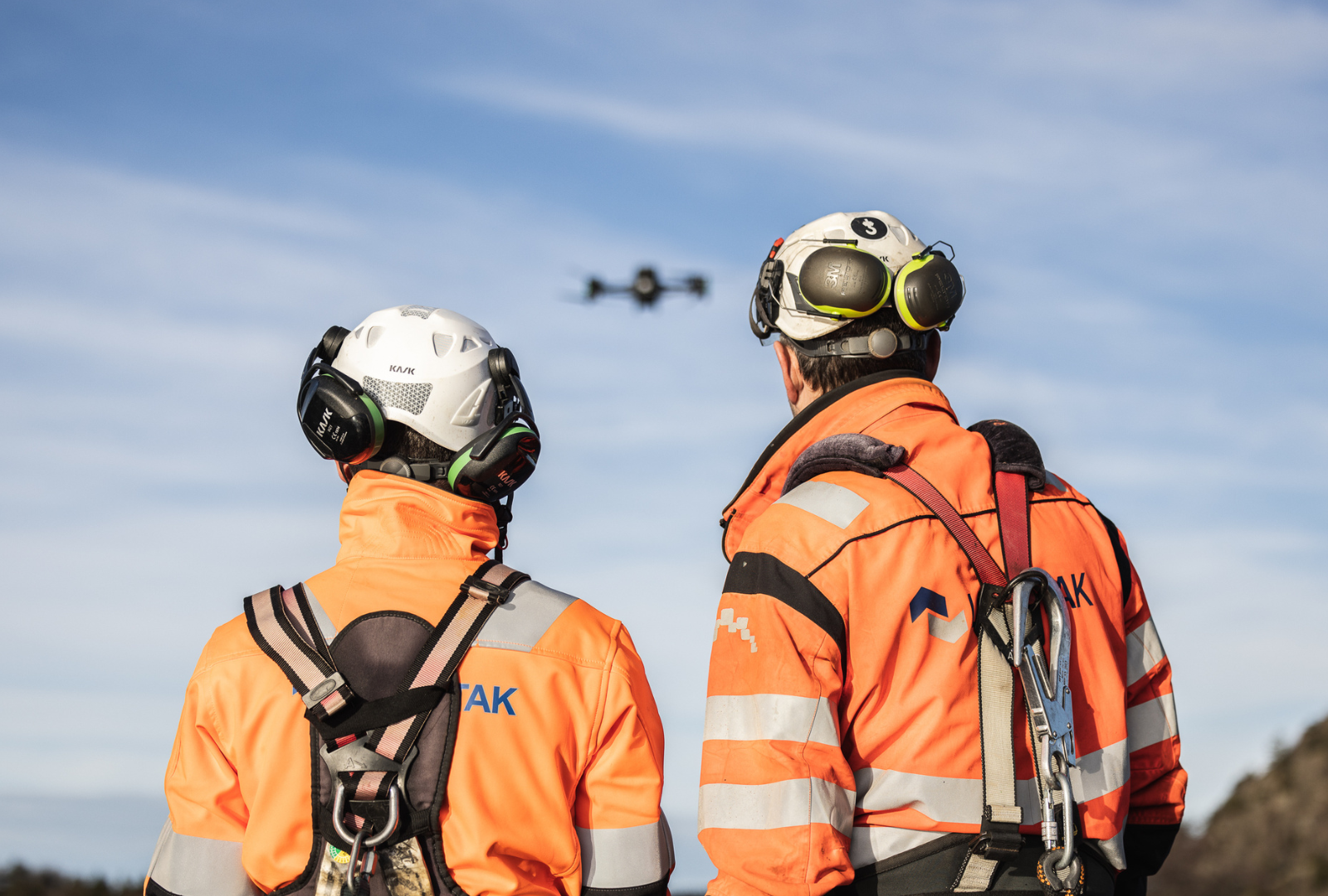 To menn med Lett-Tak-uniform ser på en drone fra et tak